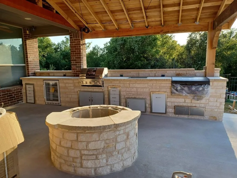 Stone outdoor kitchen with a round stone fire pit under a cedar ceiling